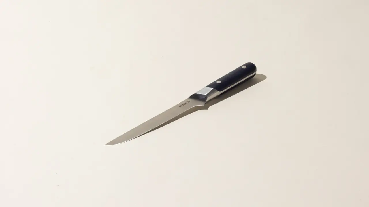 A paring knife with a black handle lies on a beige surface.