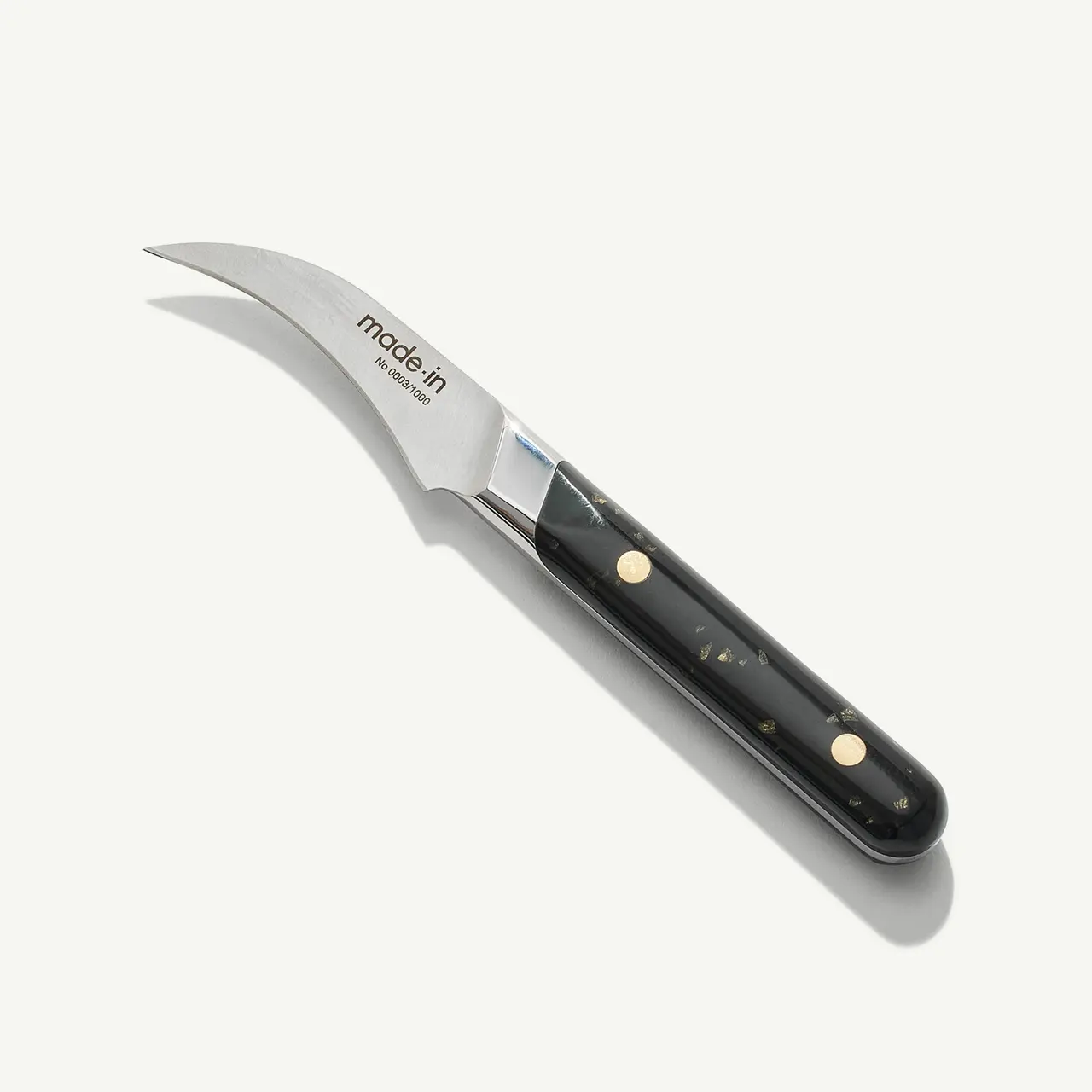 A stainless steel paring knife with a black handle and the word "made in" etched on the blade lies on a white surface.