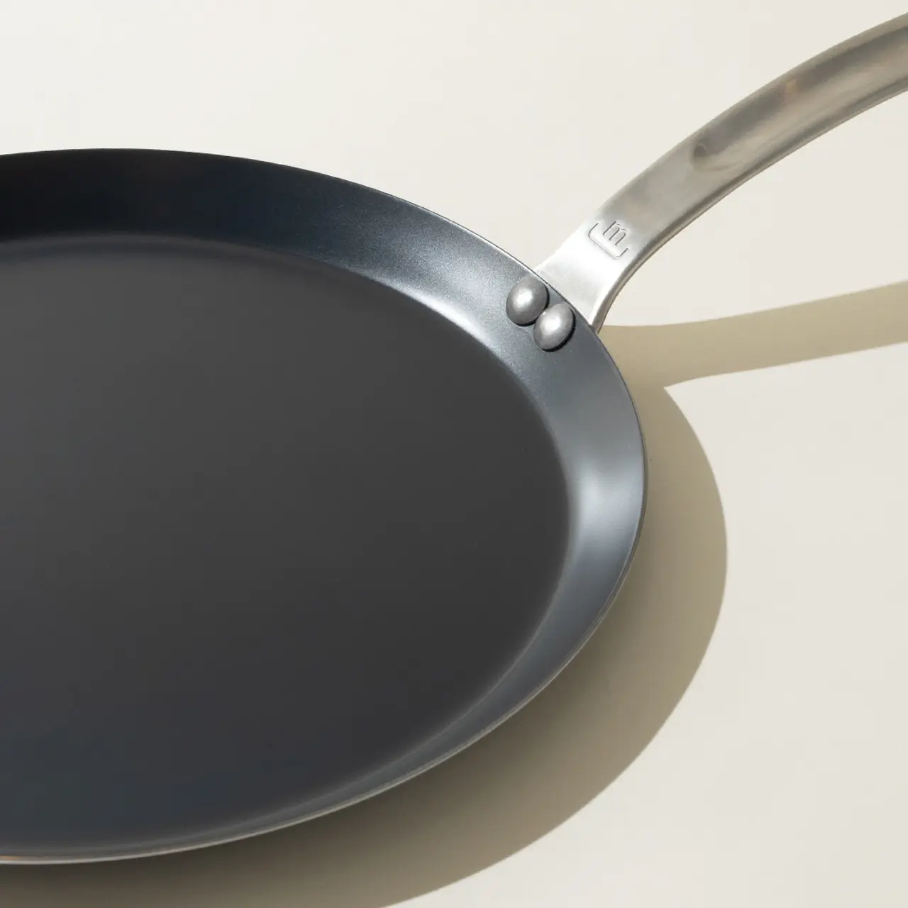 A new non-stick frying pan with a stainless steel handle on a light background, casting a soft shadow.