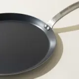 A new non-stick frying pan with a stainless steel handle on a light background, casting a soft shadow.
