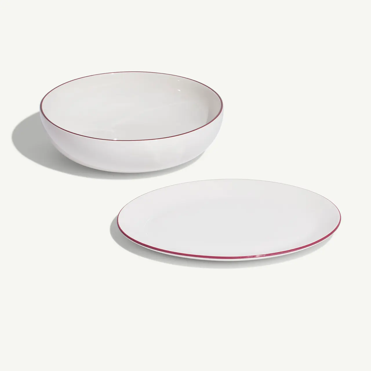 A white bowl and a plate with red trim are arranged on a light background.