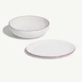 A white bowl and a plate with red trim are arranged on a light background.