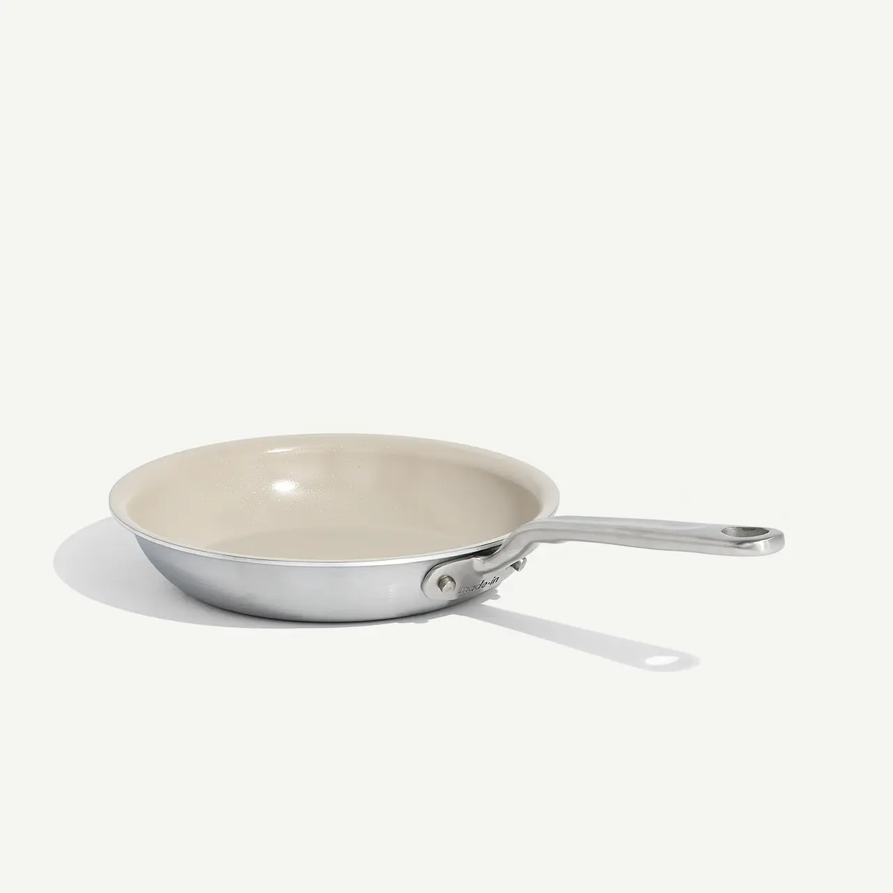 A non-stick frying pan with a stainless steel handle rests on a plain background, casting a slight shadow.