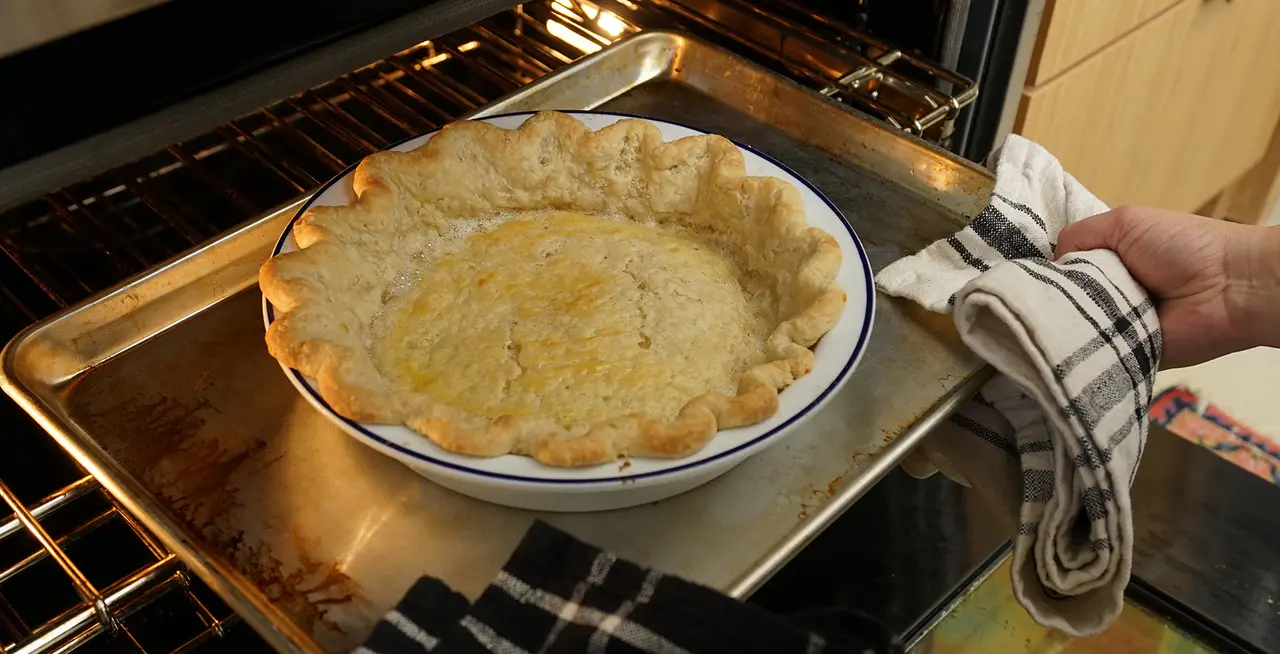 A freshly baked pie is being taken out of the oven by a person wearing a checkered oven mitt.