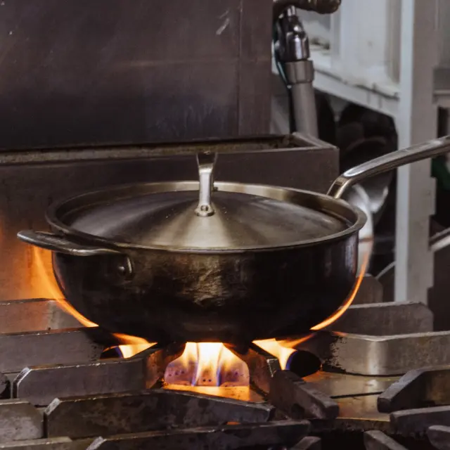 A pot with a lid is placed on a stovetop over a visible flame, suggesting cooking in a kitchen setting.