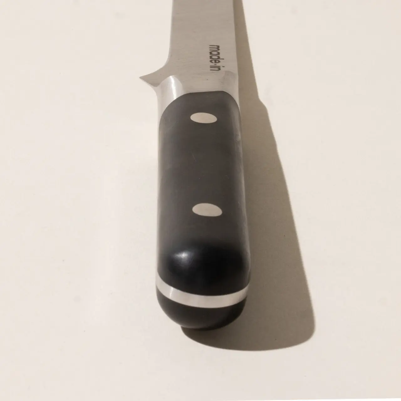 A close-up of a kitchen knife with a black handle lying on a surface.