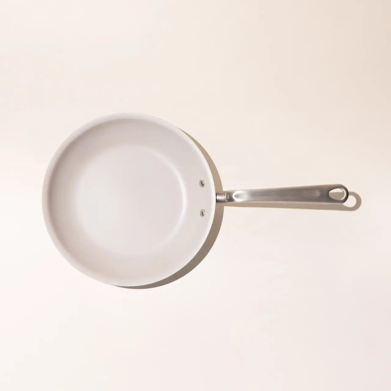 A single white frying pan with a stainless steel handle on a light background, viewed from above.