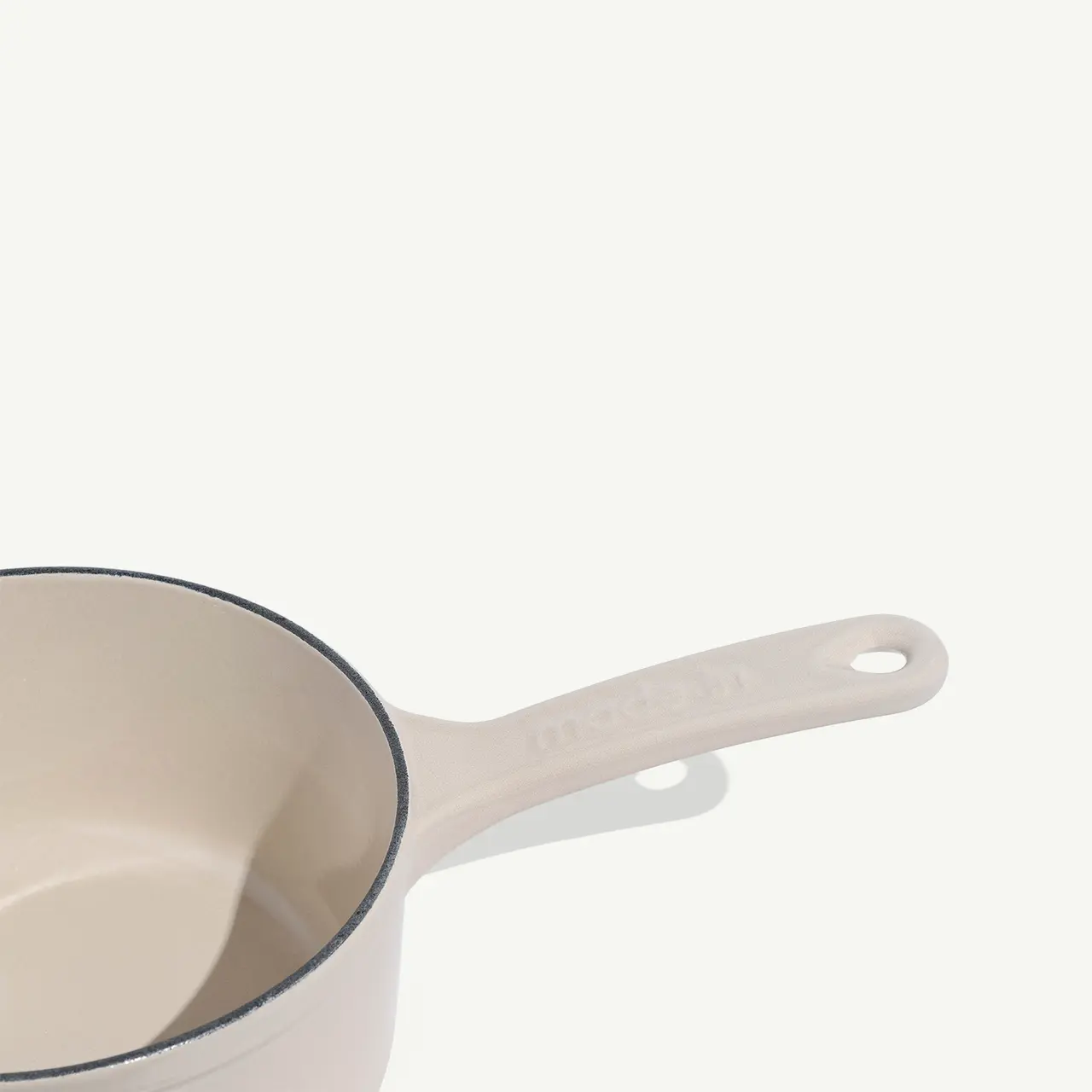 A cream-colored saucepan with a contrasting dark rim sits isolated against a light backdrop.