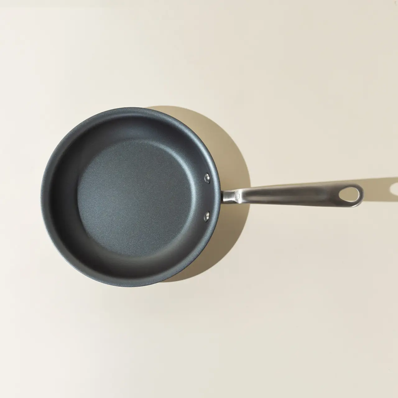 A non-stick frying pan with a metal handle is seen from above on a light background.