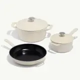 Three cookware pieces are displayed, including a large cream-colored pot with a lid, a smaller cream-colored saucepan, and a black frying pan.