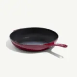 A deep red cooking pan with a black interior and a handle is positioned on a light background.