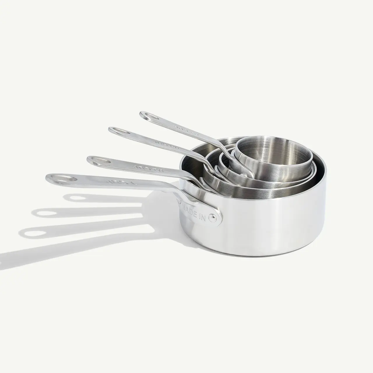 A set of nested measuring cups with metal construction and handles rests on a white surface casting soft shadows.