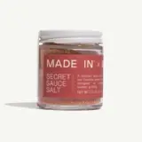 A glass jar of "Secret Sauce Salt," featuring a bold red label that highlights its use as a spice blend for enhancing summer grilling, with a net weight of 2.5 oz.