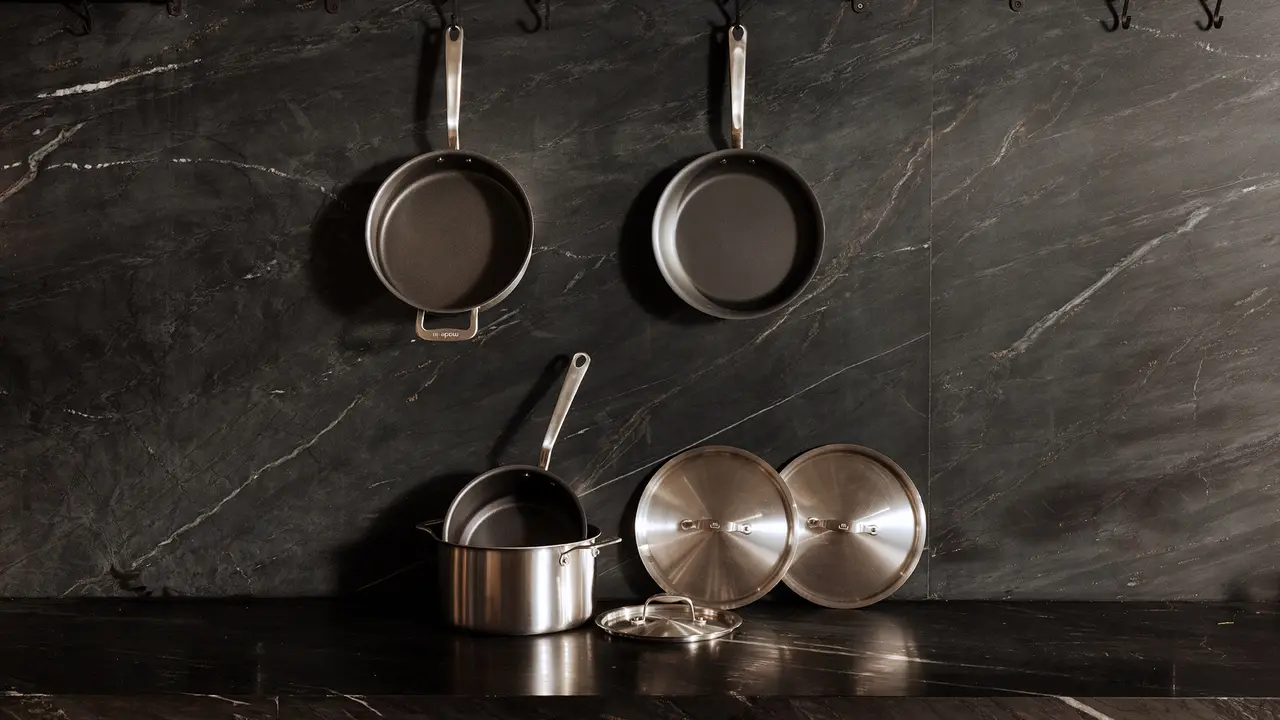 Hanging and standing stainless steel pots and pans against a dark marble background in a modern kitchen setting.