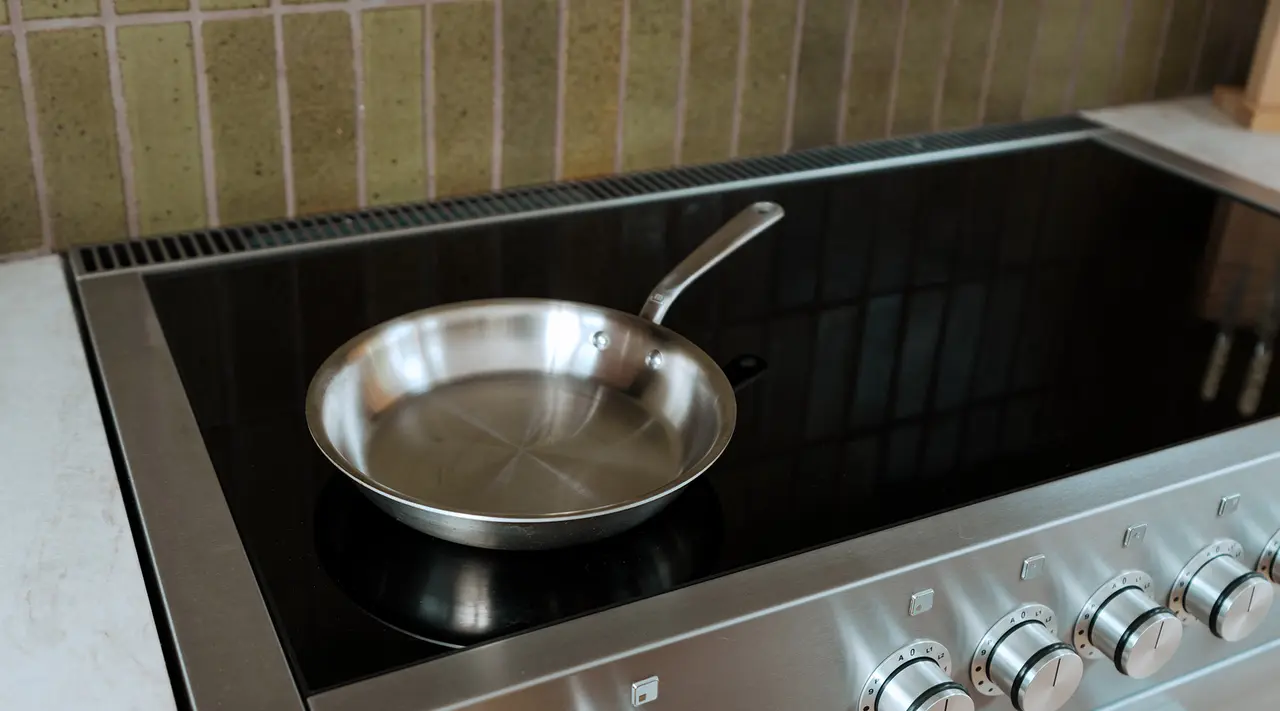 A stainless steel frying pan sits on a modern induction stove with controls visible to the right.