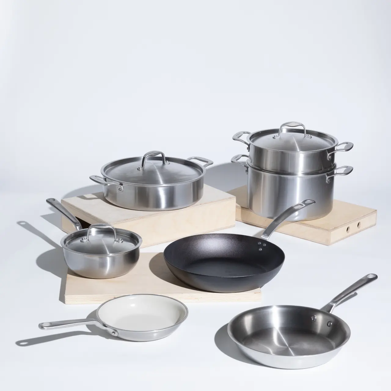 A collection of various stainless steel cookware, including pots and frying pans, arranged on a light wooden surface.