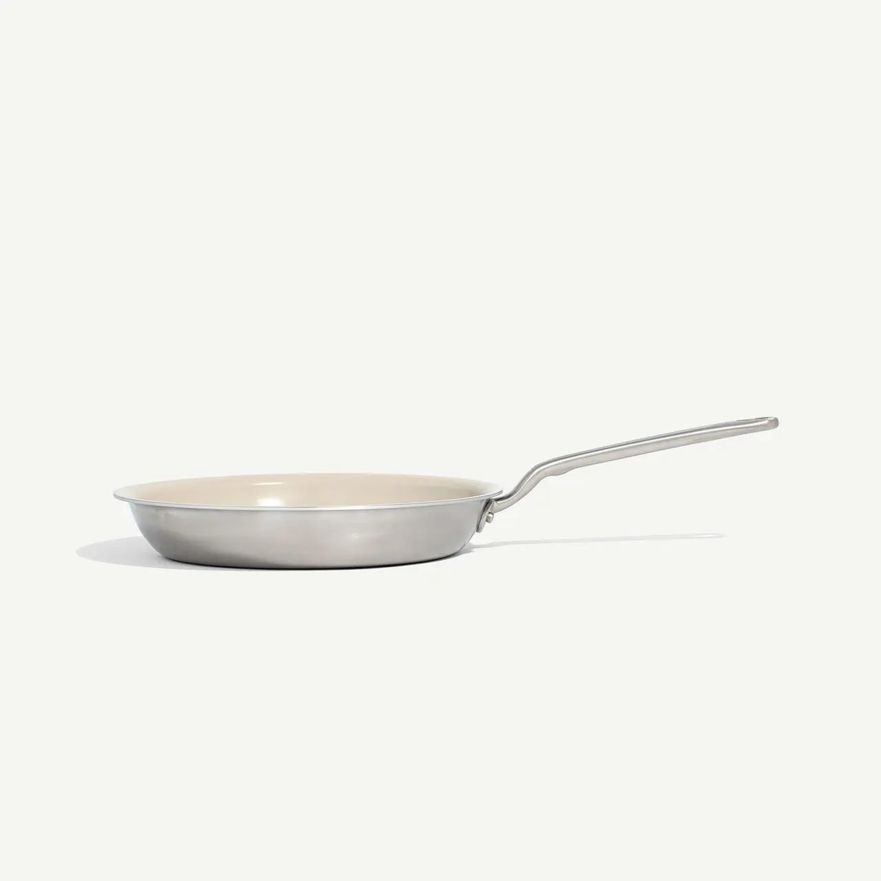 A stainless steel frying pan with a long handle is positioned against a plain, light background.