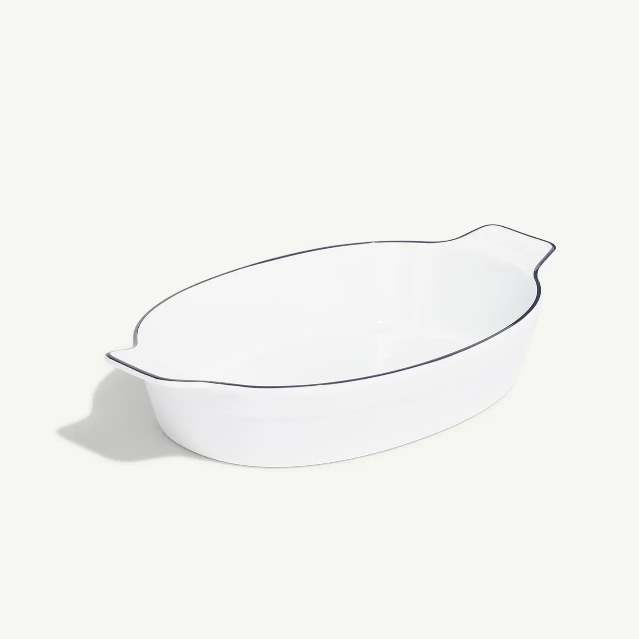 A white ceramic oval baking dish with fluted edges sits against a plain background.