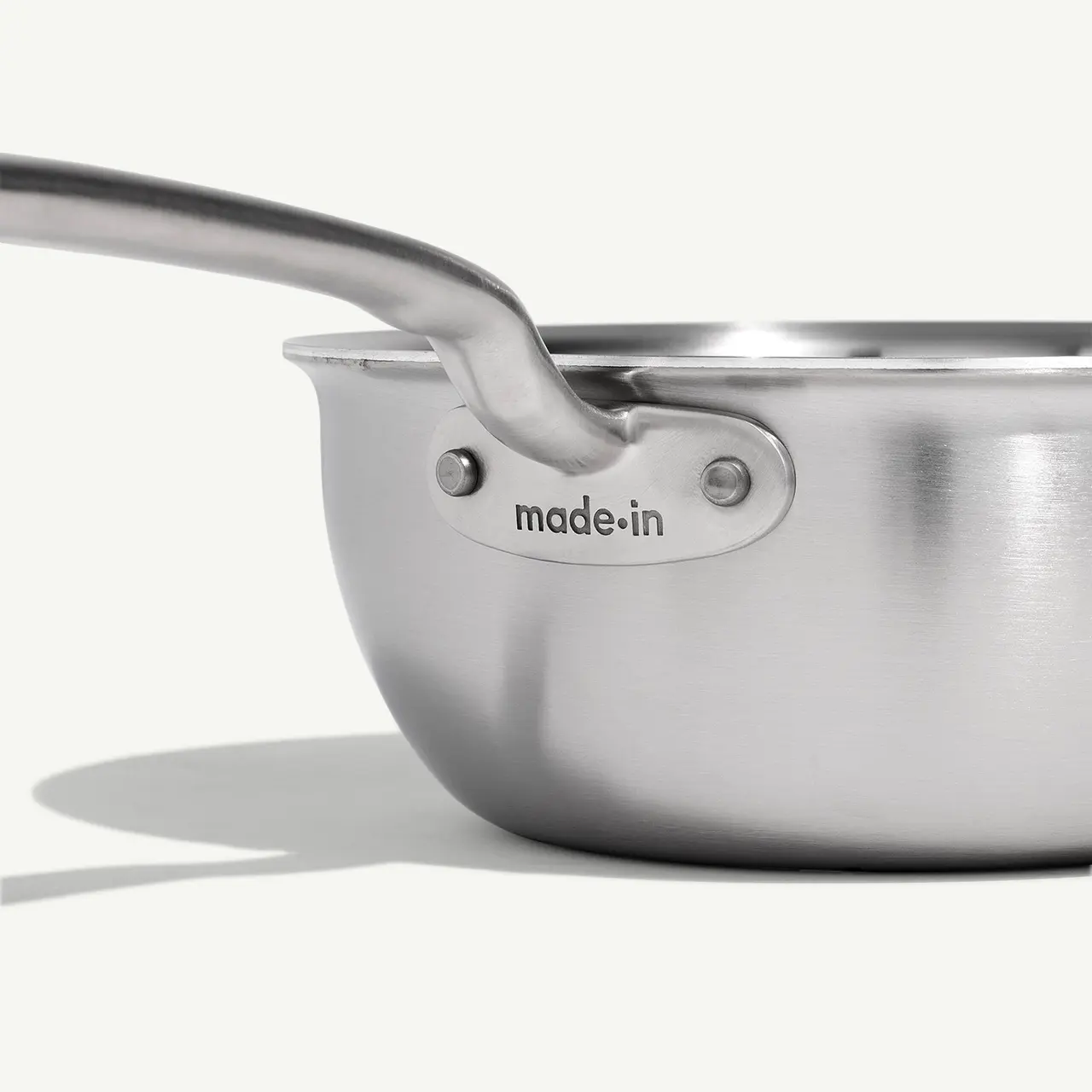 A stainless steel pot with the text "made.in" engraved near the handle, casting a shadow on a light surface.