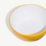 A round bowl with a bright yellow exterior and a white interior is displayed against a light background.