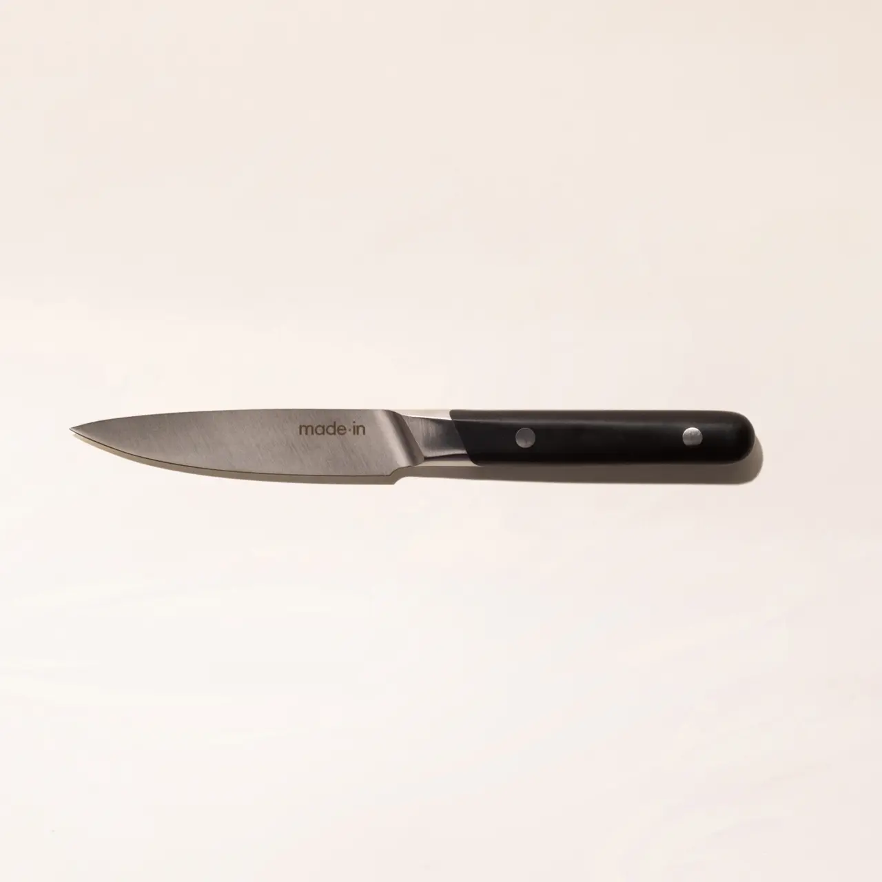 A paring knife with a black handle on a pale background.