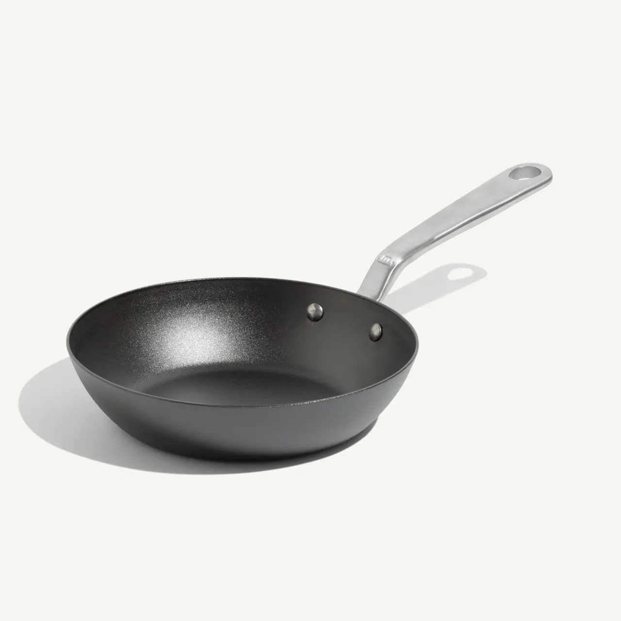 A black non-stick frying pan with a silver handle is positioned on a light background.