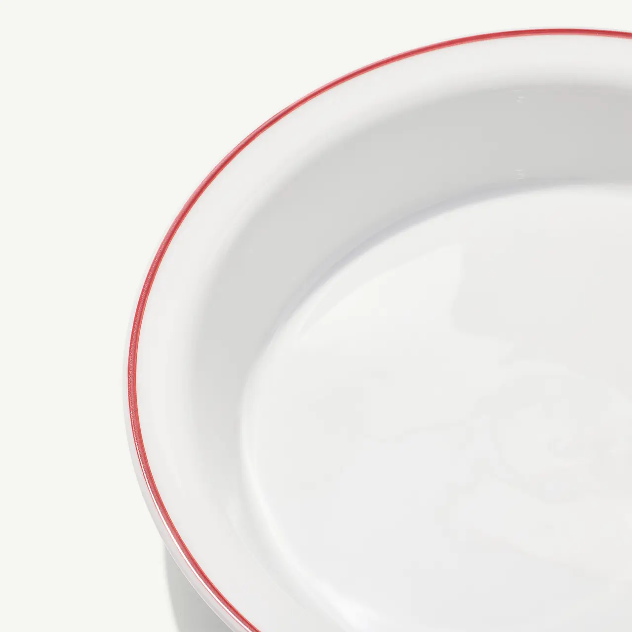 A close-up view of a white ceramic bowl with a red rim on a light background.