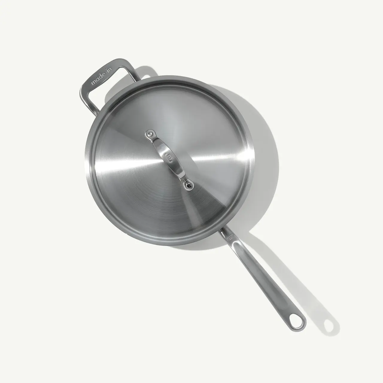 A stainless steel frying pan with a lid, viewed from above against a light background.