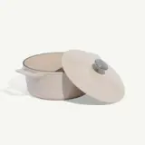 A beige Dutch oven with its lid ajar is displayed against a light grey background.