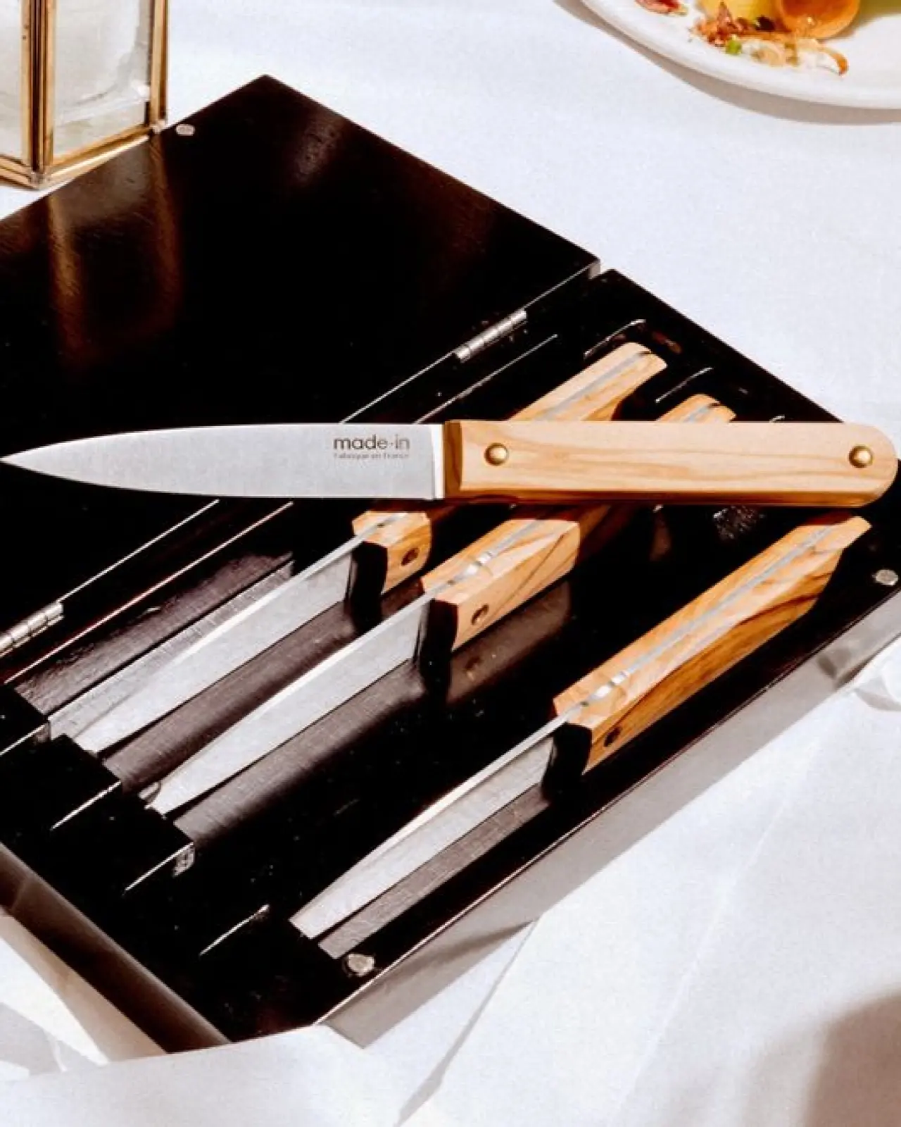 A knife block on a table contains several knives with wooden handles and one knife resting on top, partially inserted into a slot.