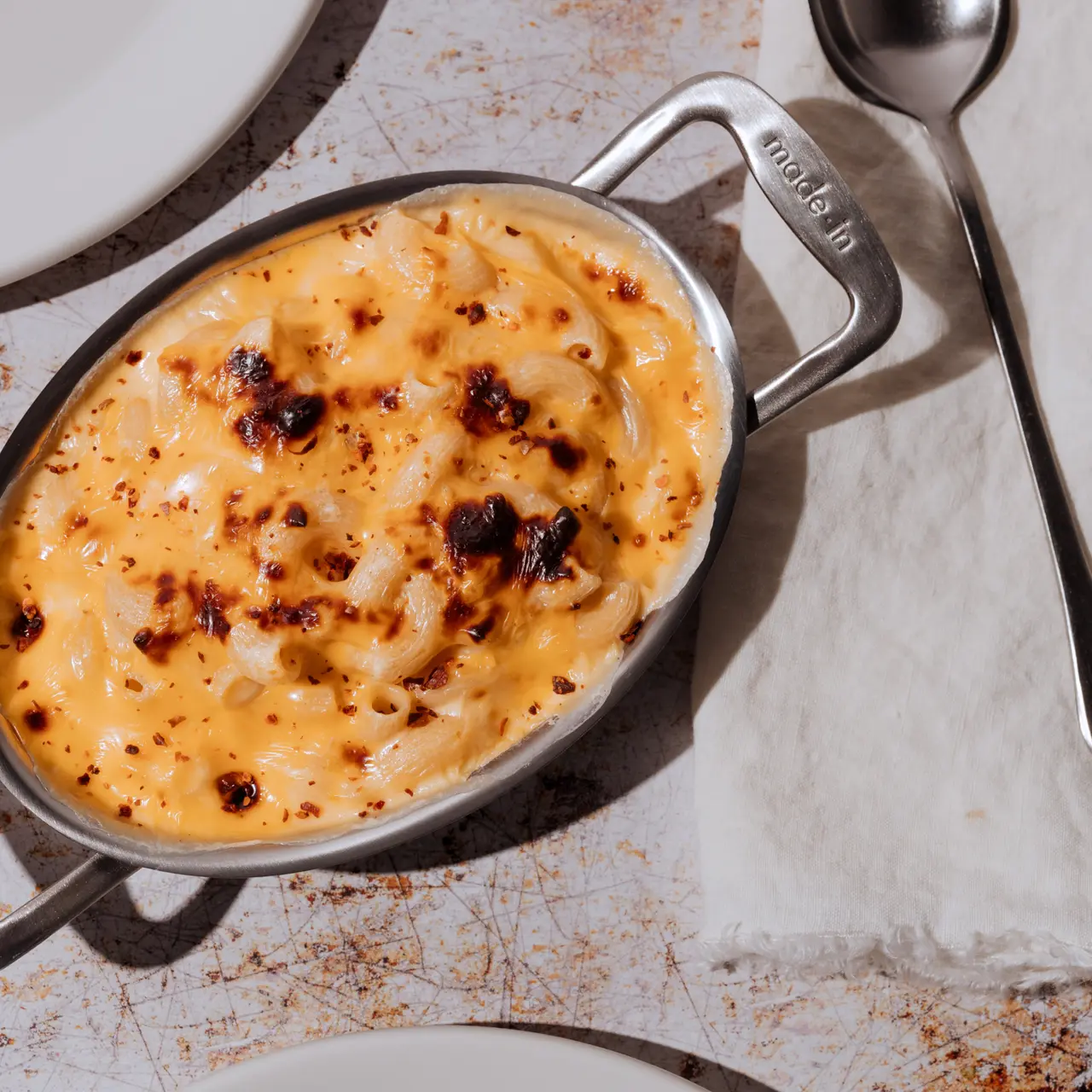 A creamy, baked mac and cheese dish with a golden, crispy topping served in a metal dish.