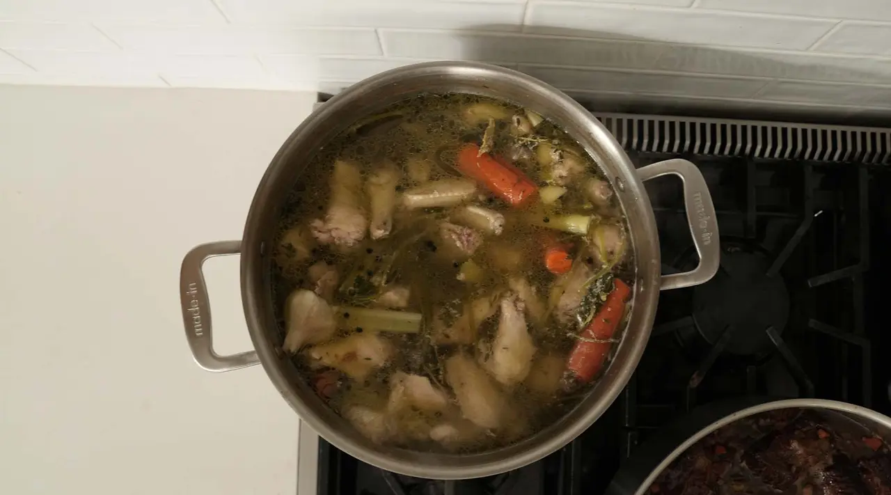 A pot of soup with various vegetables and chunks of meat simmering on a stovetop.