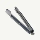 A pair of metal tongs with scalloped gripping ends is positioned open against a white background.