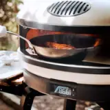 A cast-iron skillet with food is inside a portable outdoor pizza oven showing a temperature of 865 degrees Fahrenheit.