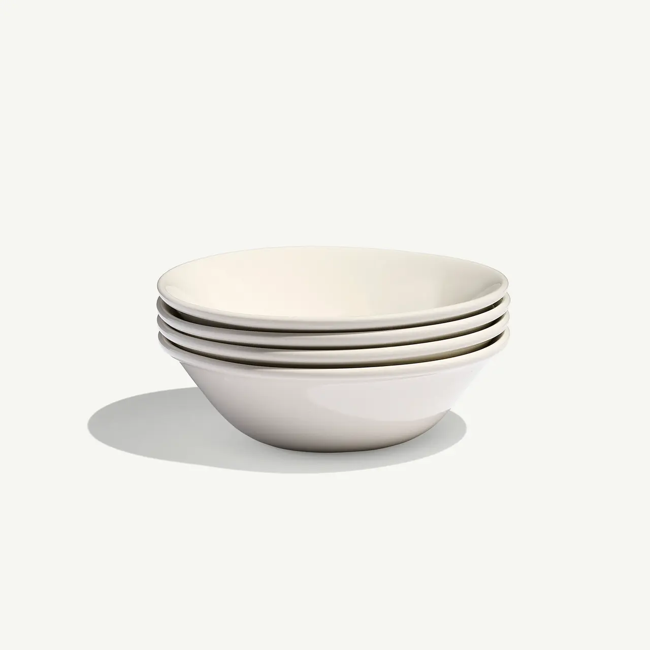 A stack of four white ceramic bowls casts a soft shadow on a light background.