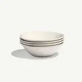 A stack of four white ceramic bowls casts a soft shadow on a light background.