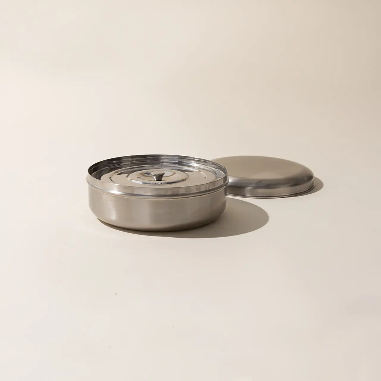 A stainless steel container with a rotating cover sits against a neutral background.