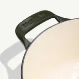 A green enameled cast iron Dutch oven with a light-colored interior and a handle embossed with "made in."