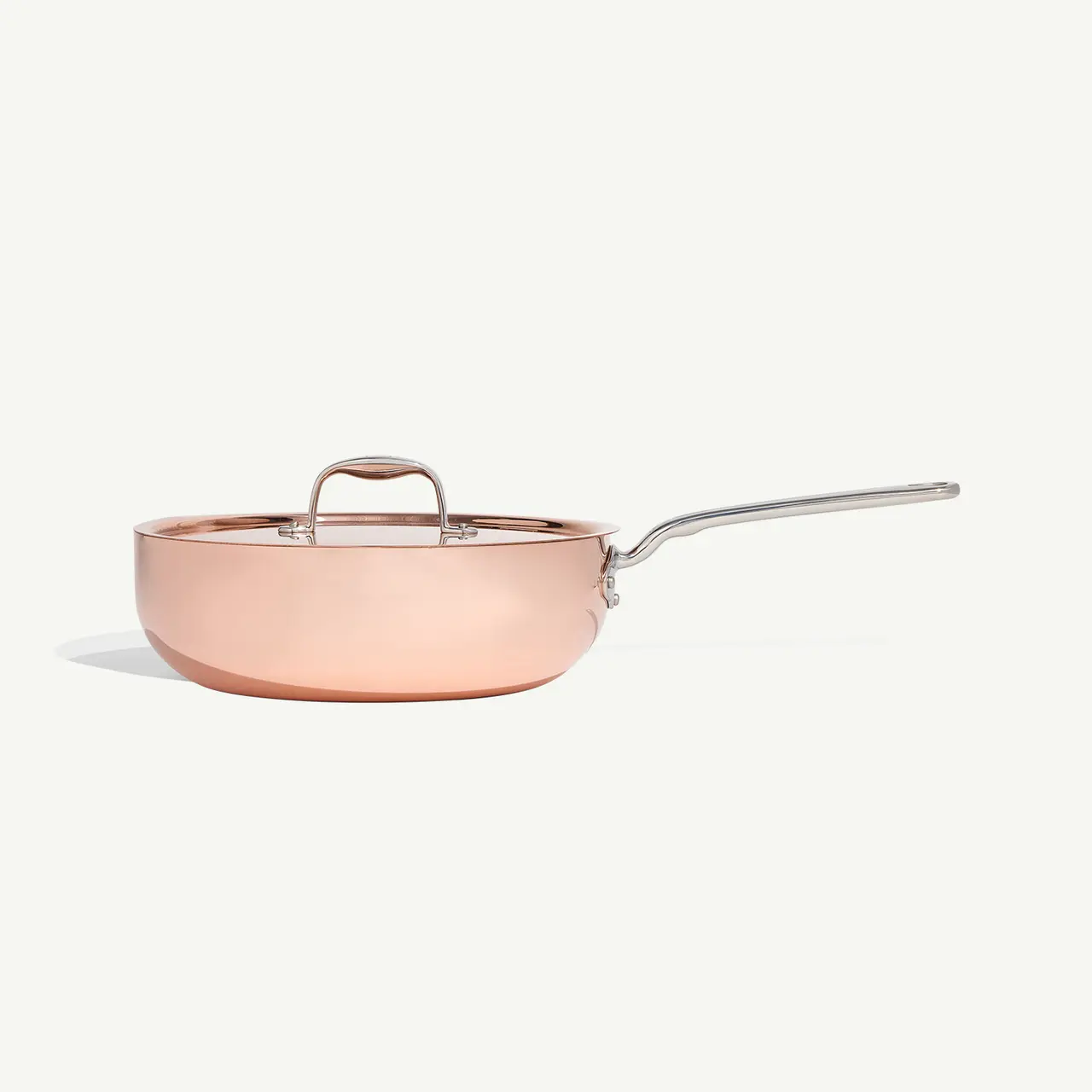 A stainless steel saucepan with a copper finish and a long handle is isolated against a white background.