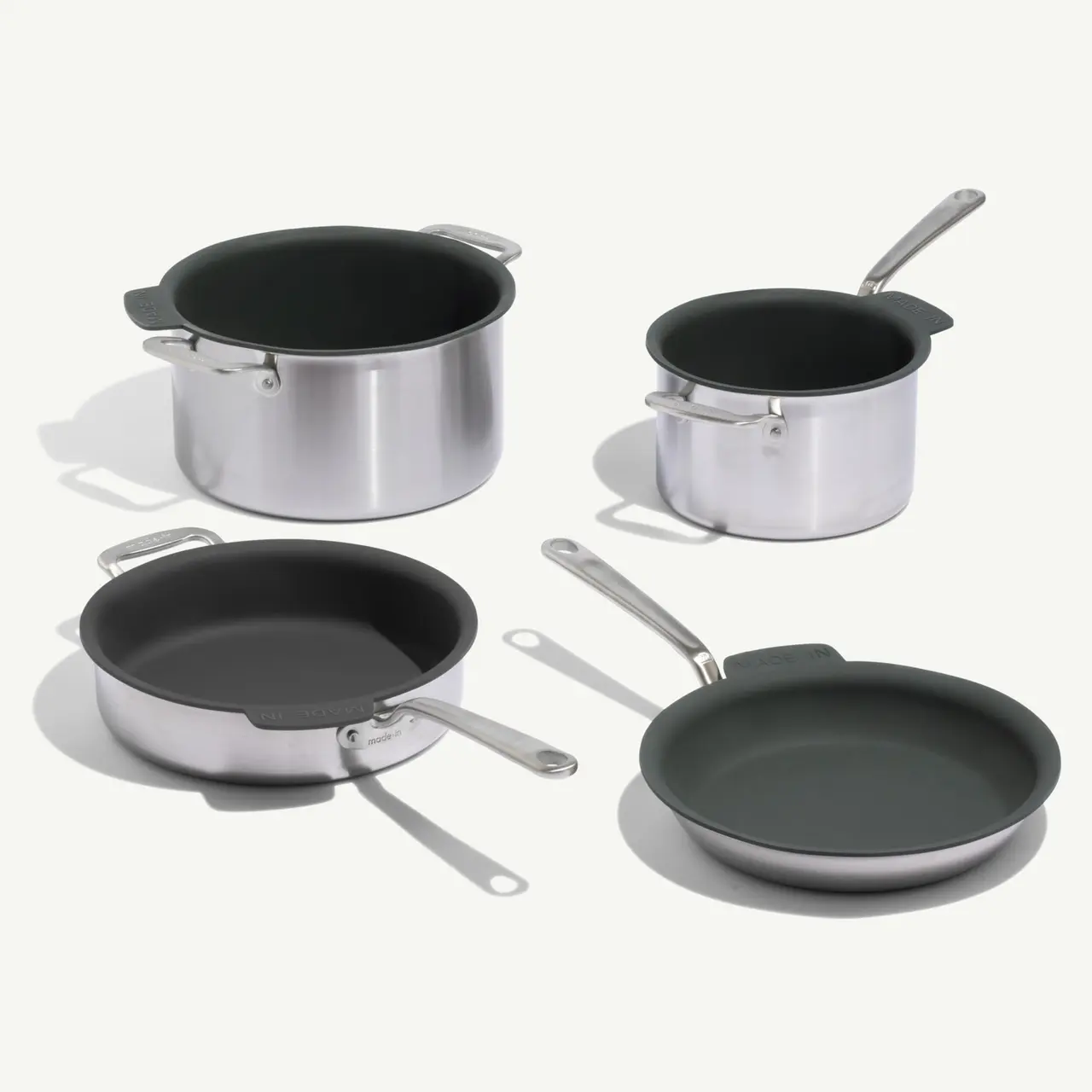 A set of stainless steel cookware featuring two pots with lids and two frying pans, all with green non-stick interiors.