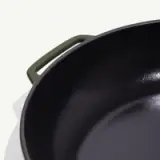 A glossy black cooking pot with a round shape and green handles.