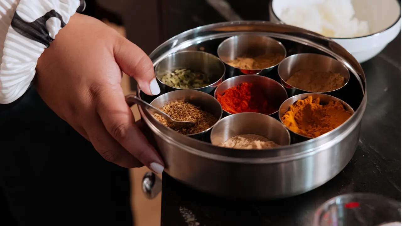A person's hand is holding a metal spice container with various colorful spices, indicating a cooking or meal preparation scenario.