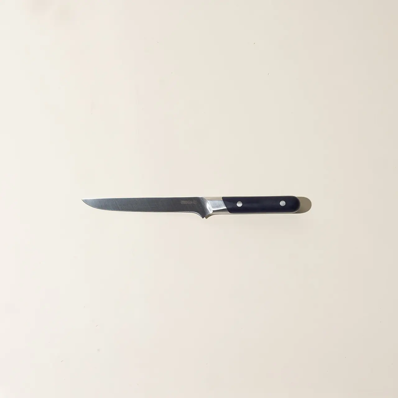 A kitchen knife with a black handle lies centered on a plain beige background.