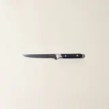 A kitchen knife with a black handle lies centered on a plain beige background.