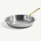 A stainless steel frying pan with a golden handle on a light background.