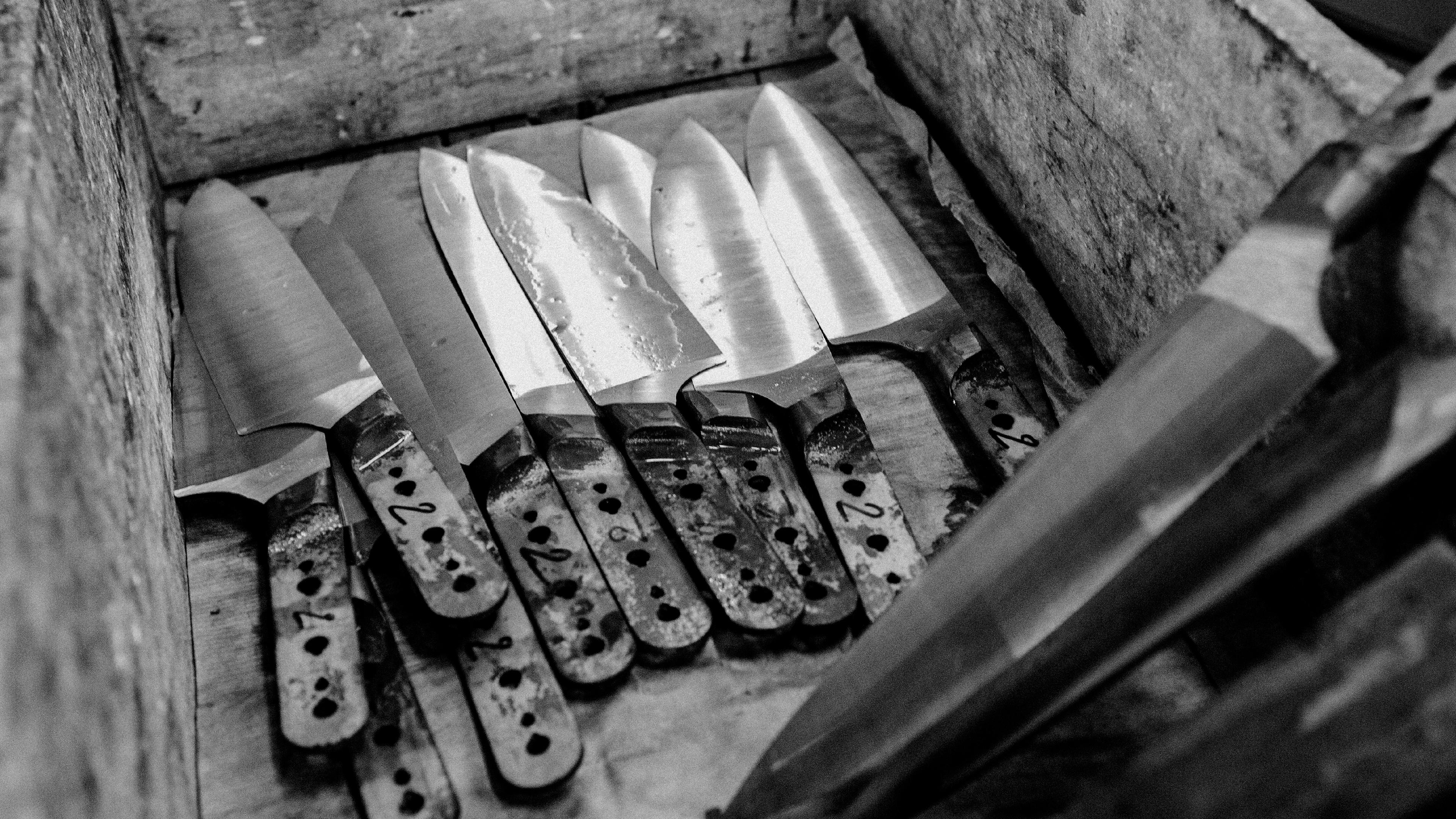 Made In kitchen knives with varied blade shapes and perforated handles rest in a wooden crate.