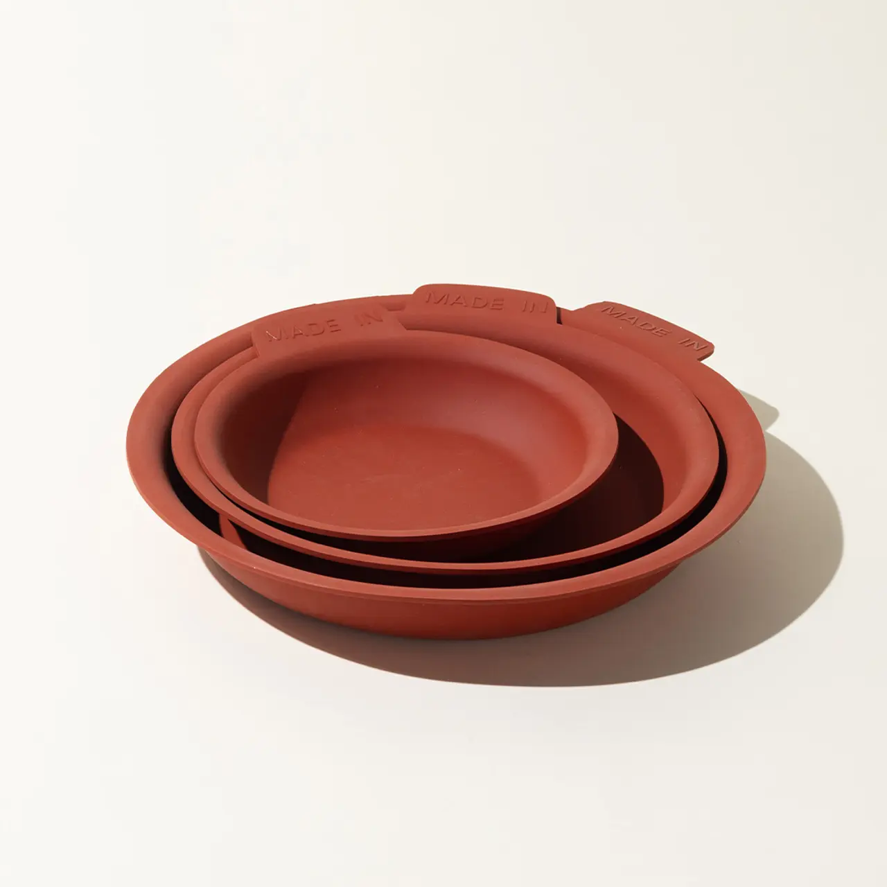 A stack of terracotta bowls in descending sizes casts a soft shadow on a white surface.