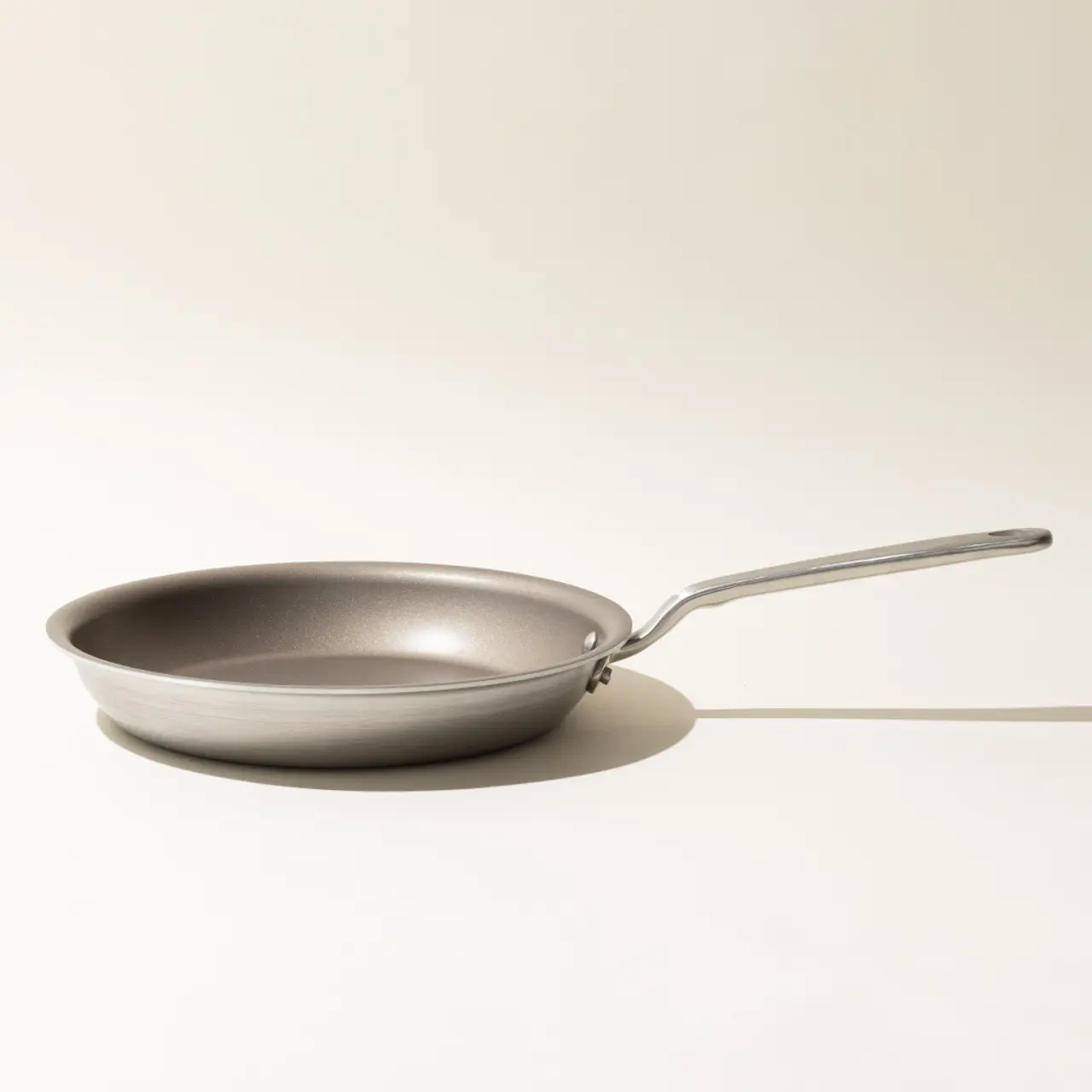 A non-stick frying pan with a stainless steel handle sits on a neutral background, casting a soft shadow to the right.