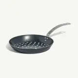 A non-stick frying pan with a perforated bottom sits against a plain background.