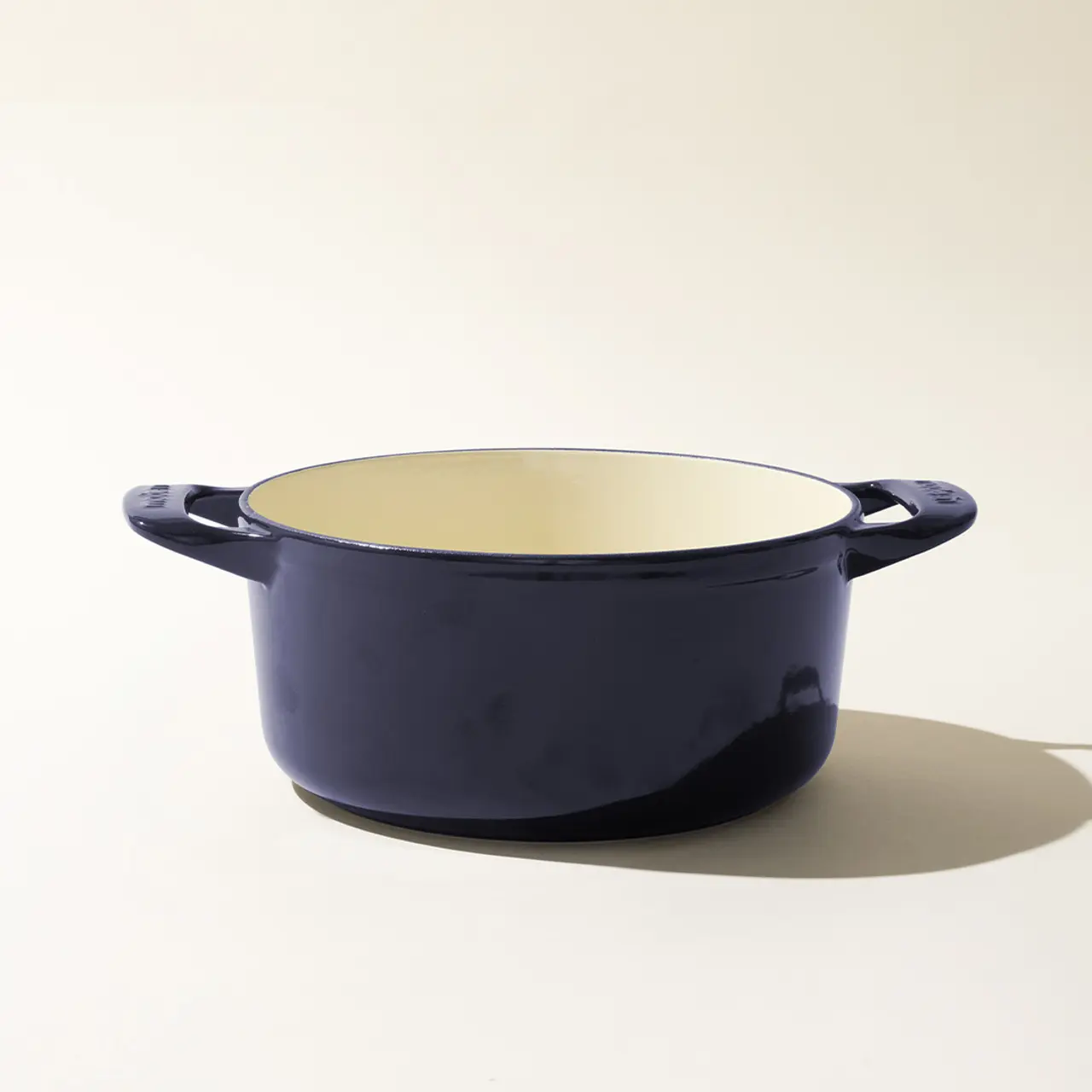 A simple navy blue enameled cast iron Dutch oven with handles, shown in profile on a light background.